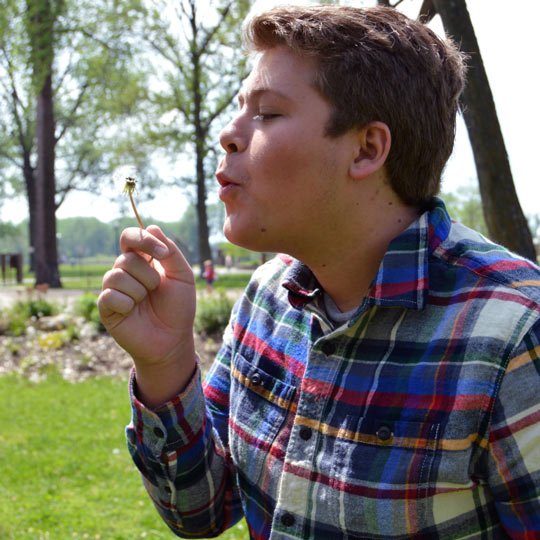 Young man blowing dandelion to the left flannel shirt