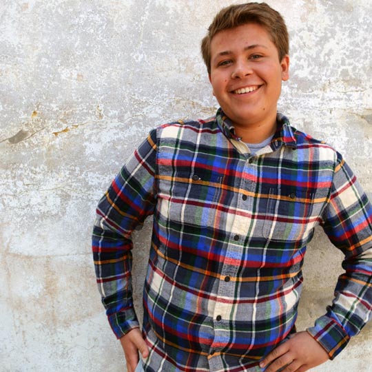 Young man in flannel shirt smiling against white wall
