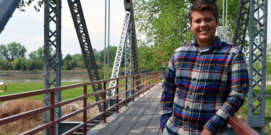 Young man in flannel shirt leaning against railing on English Landing Park bridge